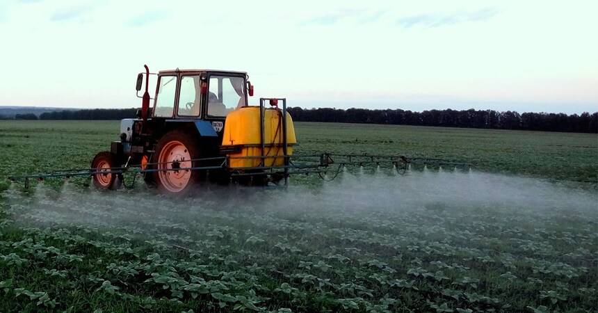 Red tractor pulling a crop sprayer across a green field at dusk