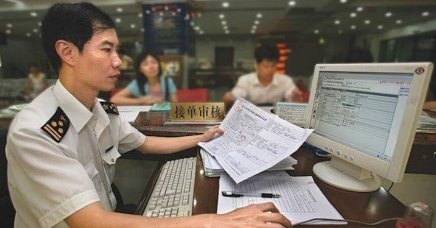 Chinese customs officer in uniform reviewing paperwork at a computer terminal