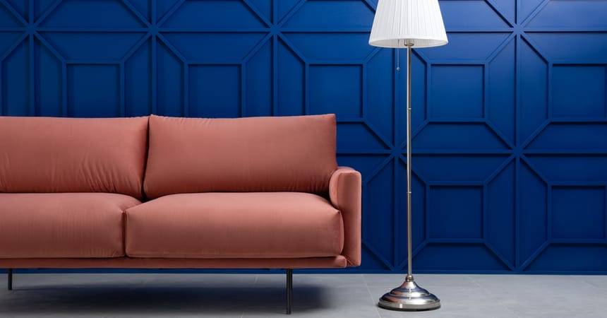 Pink sofa and floor lamp against a panelled deep blue wall