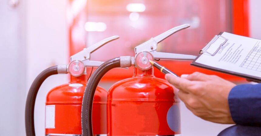 Inspector with a clipboard checking two red fire extinguishers against a wall