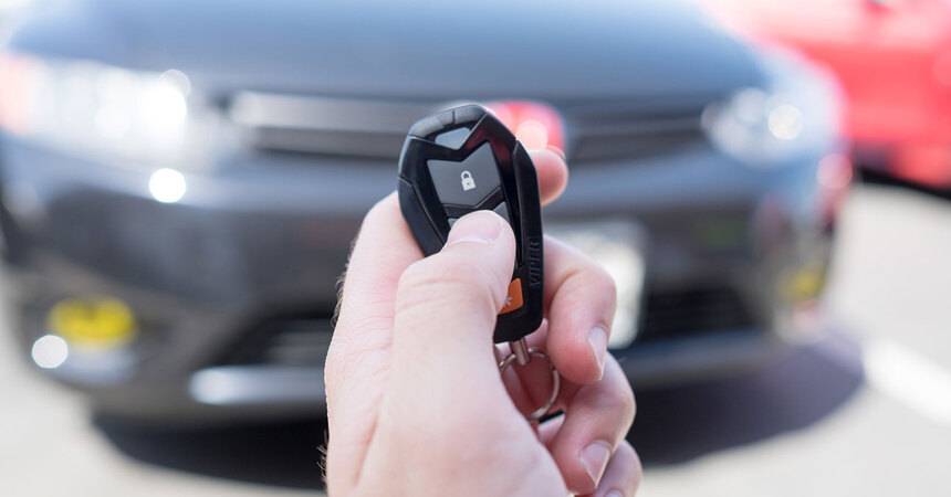 Hand pressing a car key fob remote in front of a parked vehicle