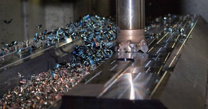 Milling head cutting a steel workpiece on a CNC machine tool, swarf across the bed
