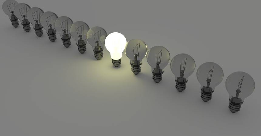Row of clear filament light bulbs on a grey surface with one lit