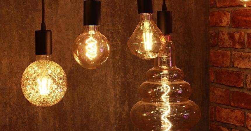 Four decorative filament pendant bulbs glowing warmly against a brick wall
