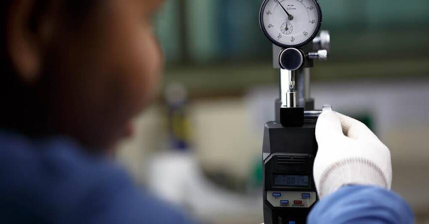 Technician in gloves reading a dial gauge on a calibration stand in a laboratory