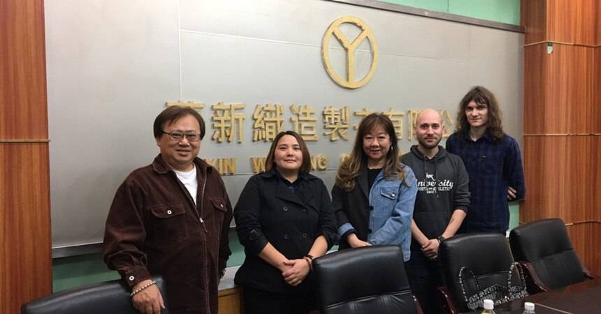 Group photograph of five people in a factory meeting room in front of a company sign