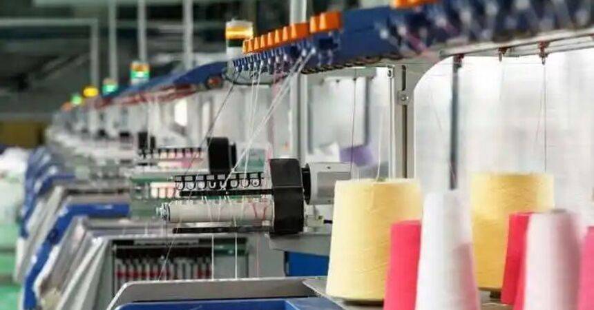 Row of industrial knitting machines with coloured yarn cones in a textile factory