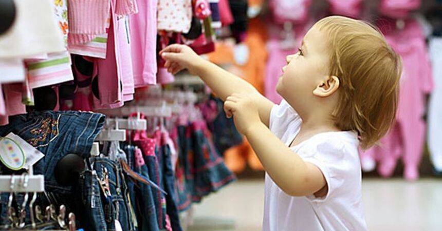 Toddler reaching for children's clothes on a rail in a shop