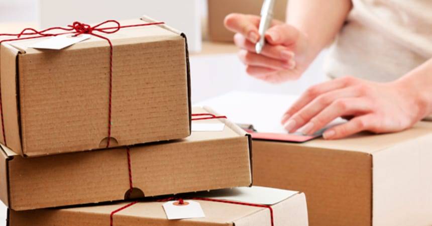 Stack of cardboard parcels tied with red string beside a person filling in paperwork