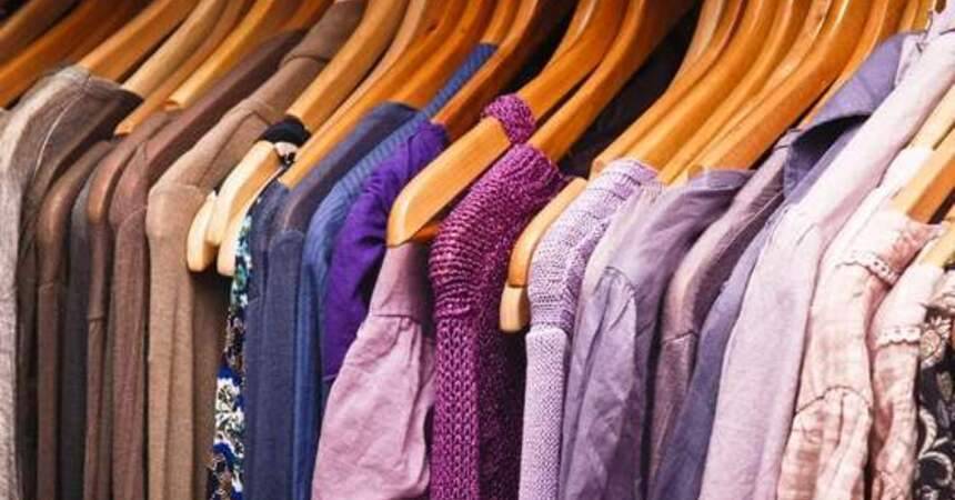 Row of coats and knitwear in muted colours hanging on wooden hangers