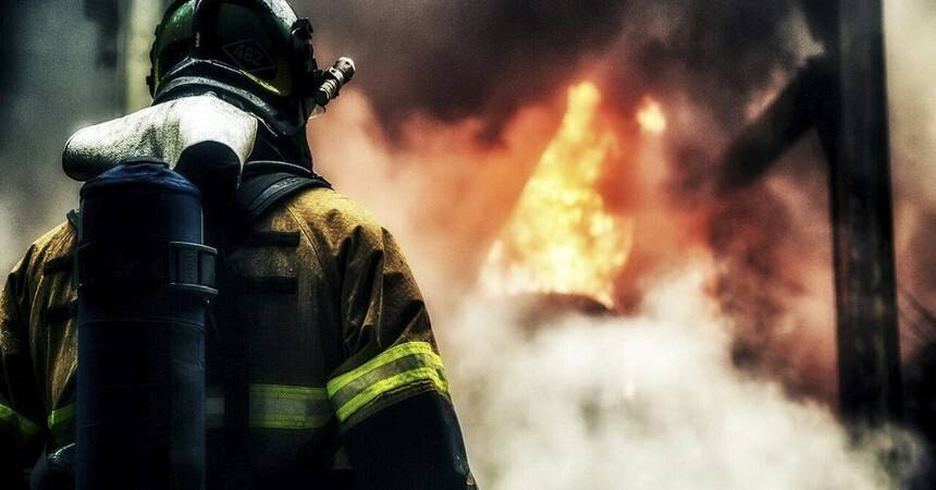 Firefighter in breathing apparatus and helmet silhouetted against flames and smoke