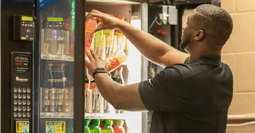 Person restocking bottled drinks into an illuminated glass-fronted vending machine